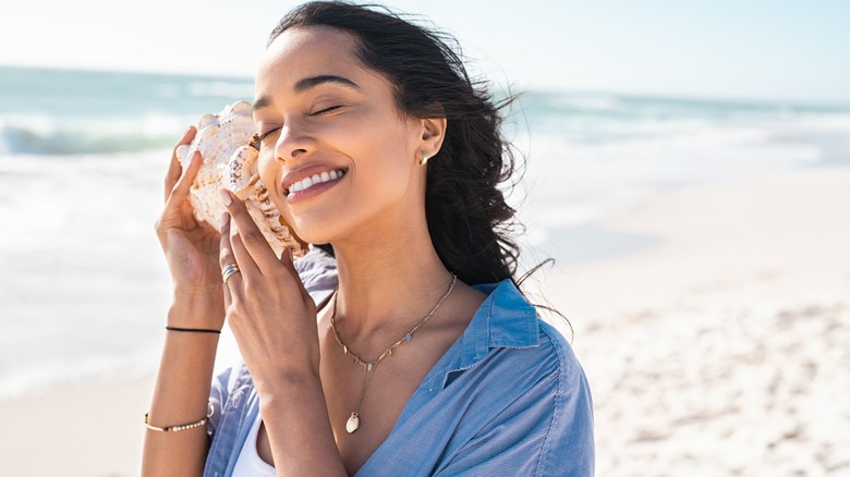 woman daydreaming with shell at the beach