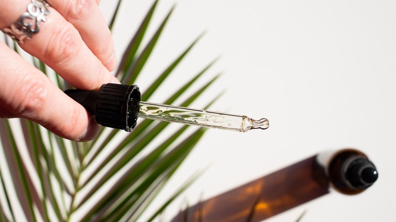 hand holding dropper of skincare serum over hemp plant