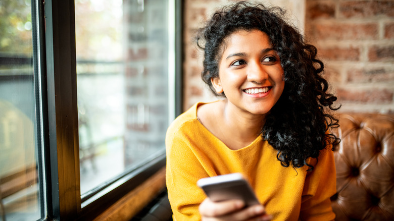 woman with curly hair sitting holding phone