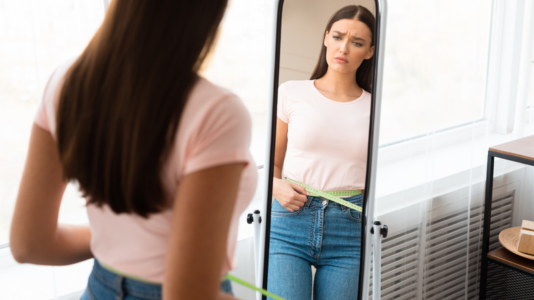 Woman frowning at body in mirror