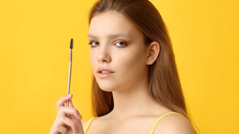Woman with bleached brows holding a brow brush
