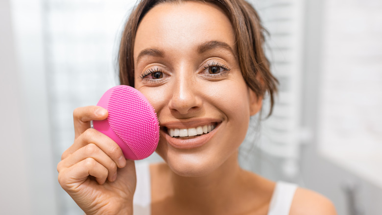 Woman using pink facial cleansing brush