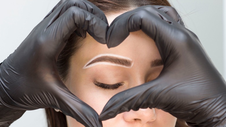 Heart-shaped hands forming a frame around a woman's eyebrow