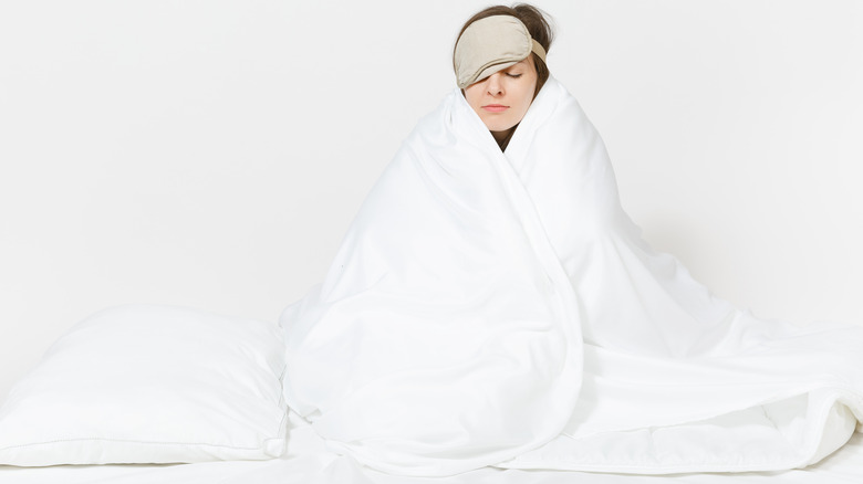 woman wrapped in a thick blanket wearing an eye mask