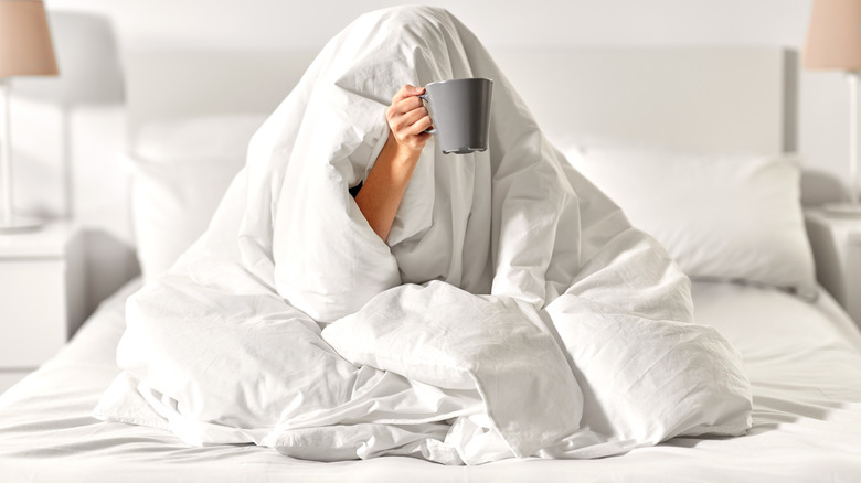 woman completely wrapped in a blanket with only her hand holding a mug sticking out