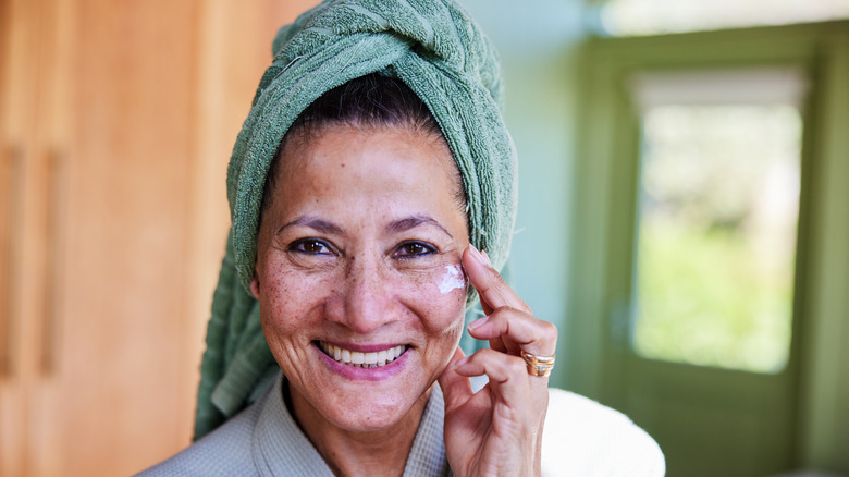 Smiling older woman applying moisturizer