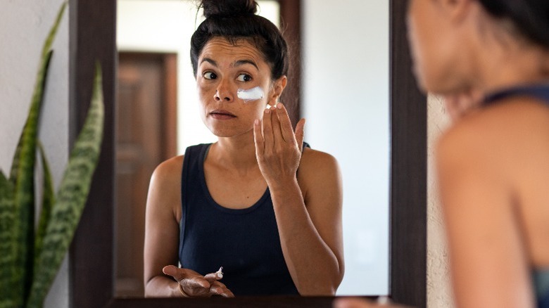 Woman applying sunscreen to face in mirror