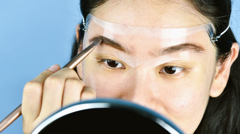 Woman applying makeup with eyebrow stencil