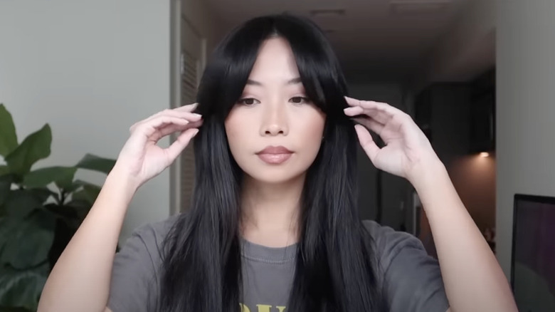 A woman arranges her curtain bangs for the camera.