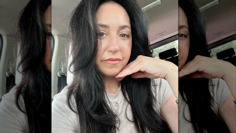 A woman with long dark layered hair taking a selfie in a car.