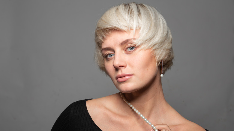 A woman posing with a platinum-blond bixie cut and dangle pearl earrings..