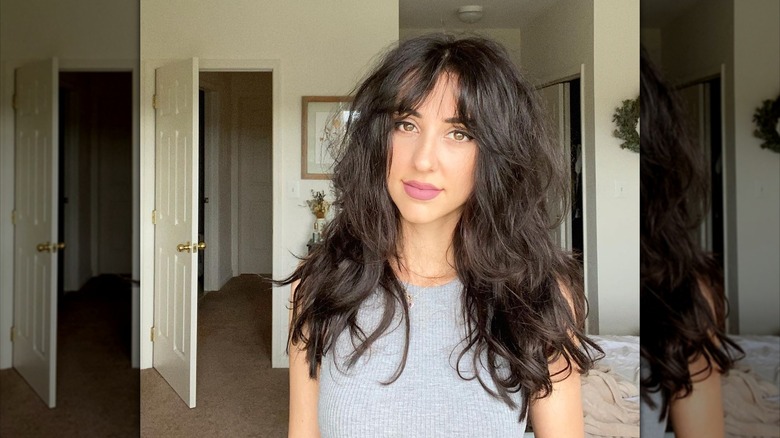 A person with a dark textured shag haircut posing at home.