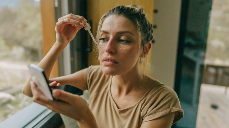 Woman applying face oil in mirror