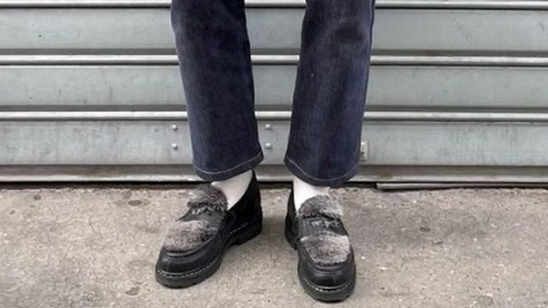 Close up of person wearing jeans and fur loafers 