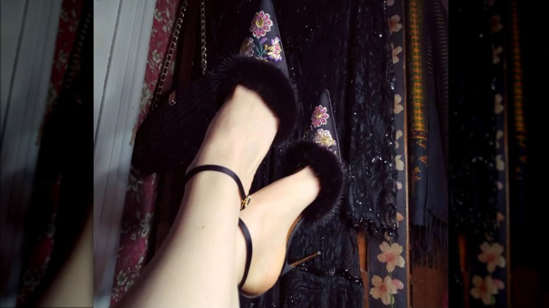 Closeup of feet wearing black fur trimmed embroidered heels 