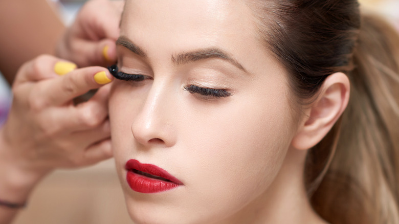 Woman with red lipstick getting false lashes applied