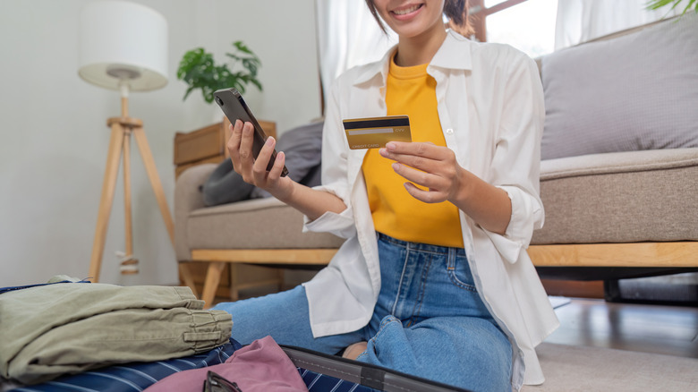 Young Asian woman making online purchases on her phone and holding her credit card