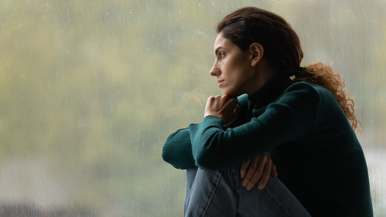 young woman with curly hair leans against rainy window thinking