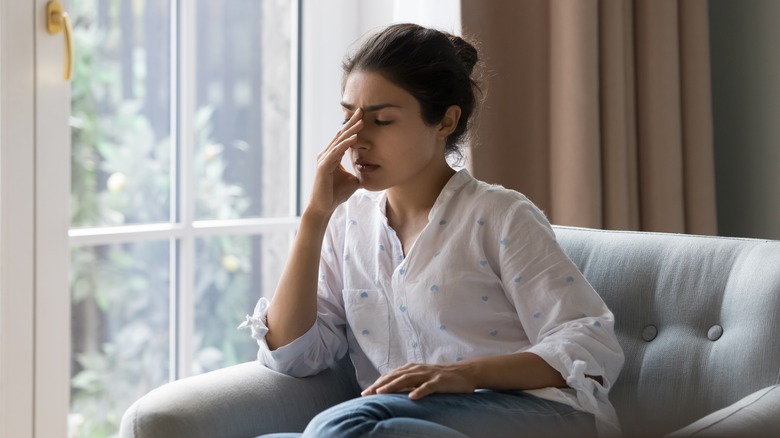 a tired woman sits in a chair by a window, her hand on her face