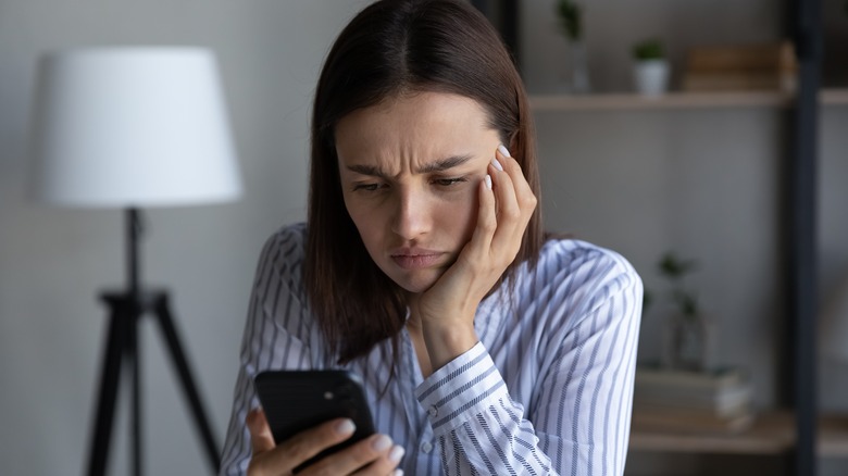 a young woman frowns at her phone