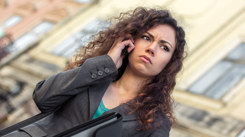 young upset woman with curly hair holds mobile phone to her ear