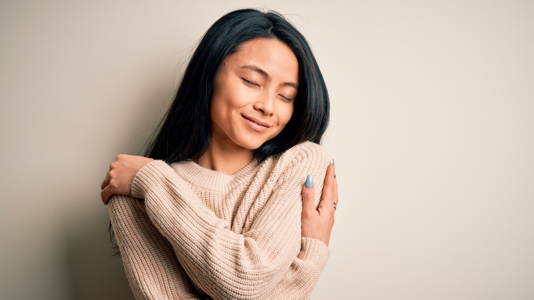 Smiling young woman hugging herself