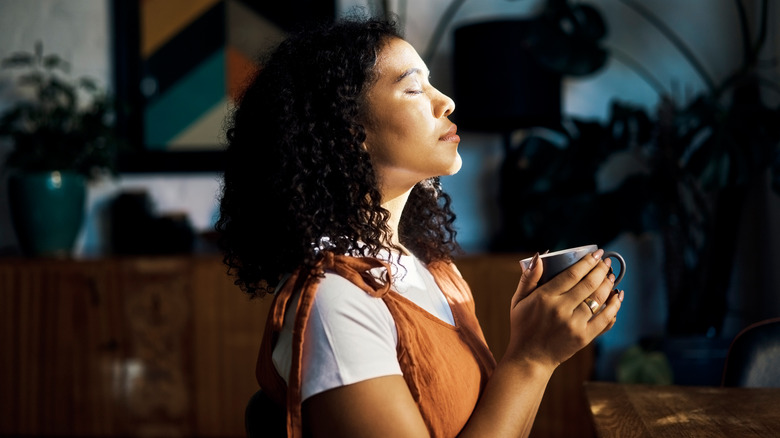 Woman deep breathing while holding ceramic mug