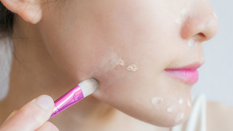 woman applying concealer to blemishes