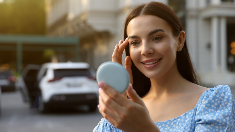 Woman looking in handheld mirror outside