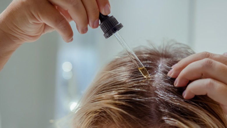 Close-up of person applying hair oil to scalp