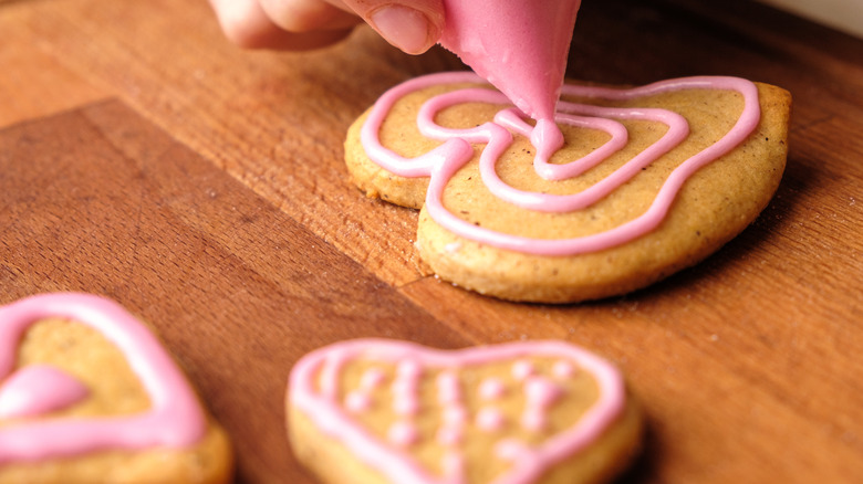 Close up of hand piping icing on Valentine cookie