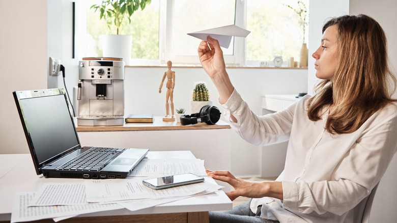 Woman playing with paper airplane in front of laptop