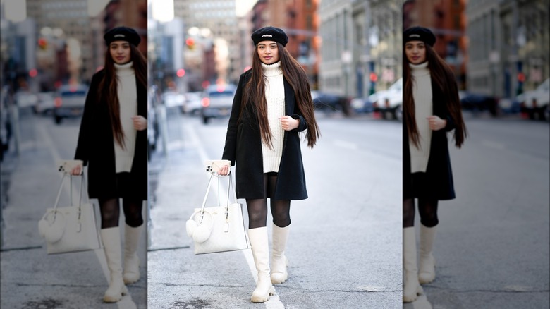 Woman wearing white knit dress, black coat, white boots