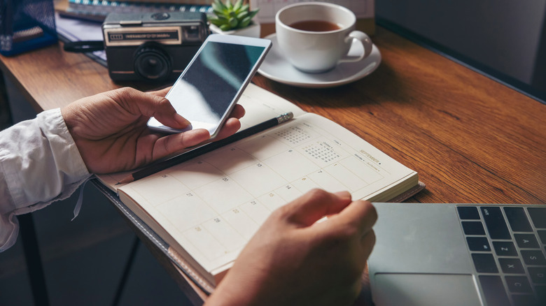 Person holding phone and planner at desk