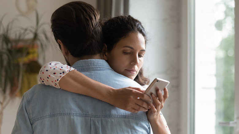 Woman secretly using phone while hugging man