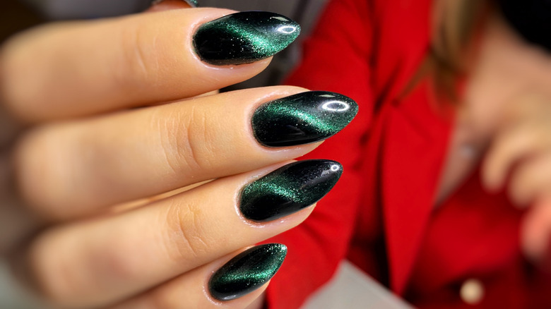 A green-and-black cat-eye manicure on long nails.