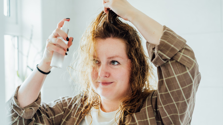 A woman applying a spray product to her damp hair