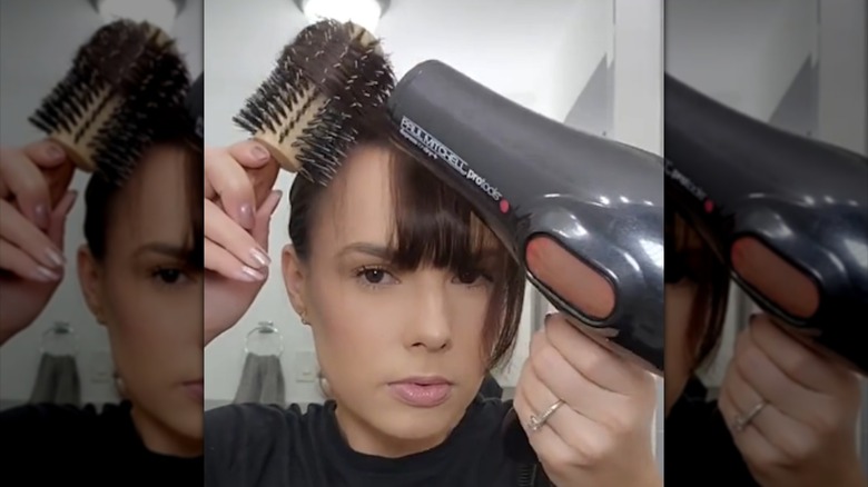 A woman blow drying sections of her bangs