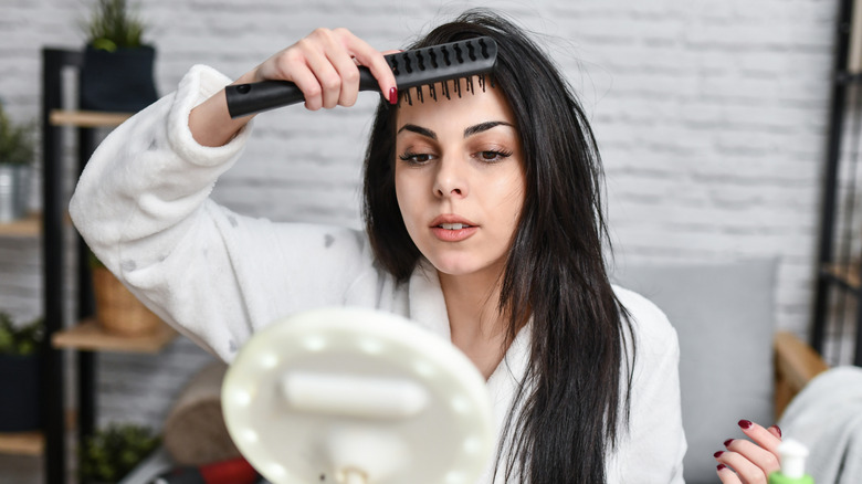 A woman looking in the mirror as she tries to style her bangs with a comb