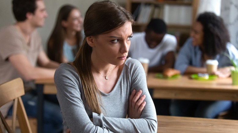 upset girl with friends laughing in background