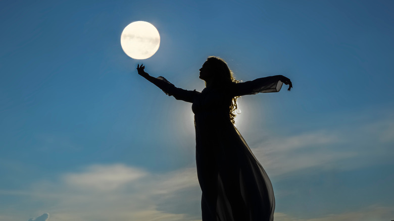 woman reaching toward full moon