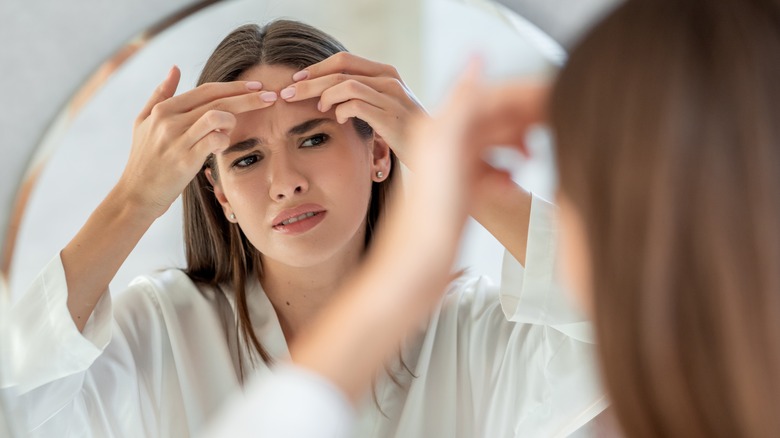 Young woman looking at her forehead acne in the mirror