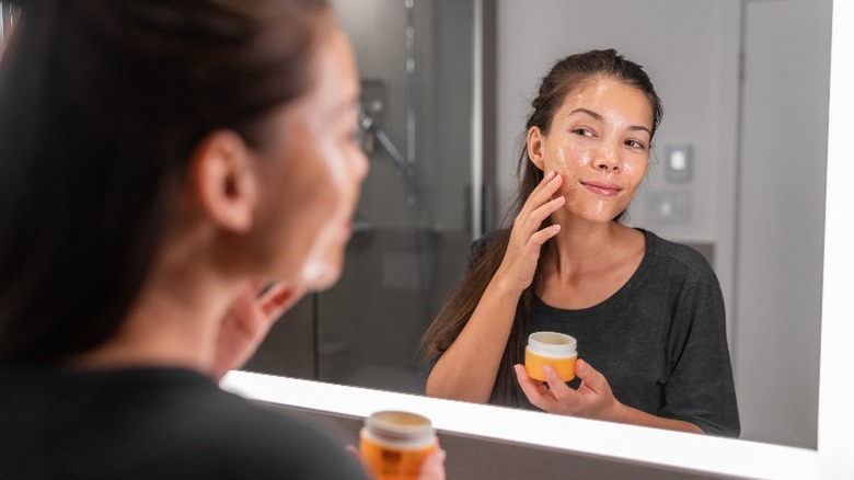 Woman applying lotion to face in mirror