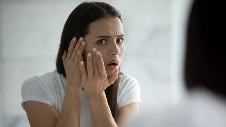 concerned woman touching face in front of mirror