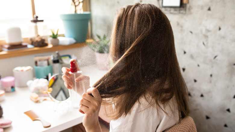 A woman applying spray to her hair.