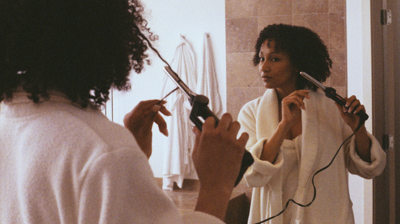 A woman curling her hair with a curling wand.