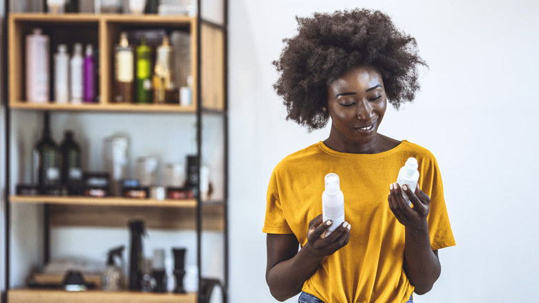 A woman holding hair care products in her hands.