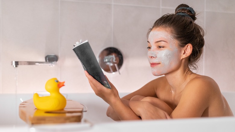 Woman in her bath reading with a clay face mask