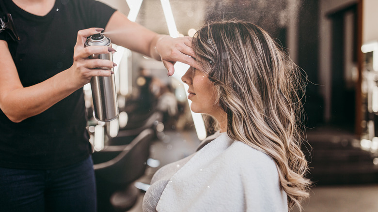 stylist applying hairspray to hair