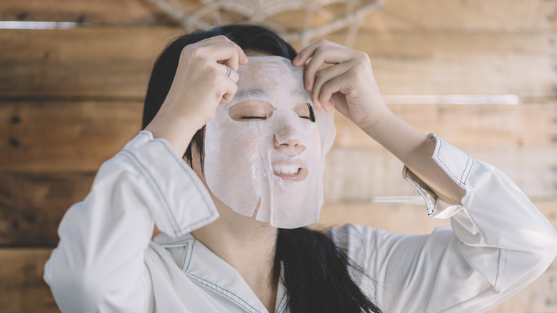 Young woman applying facial sheet mask